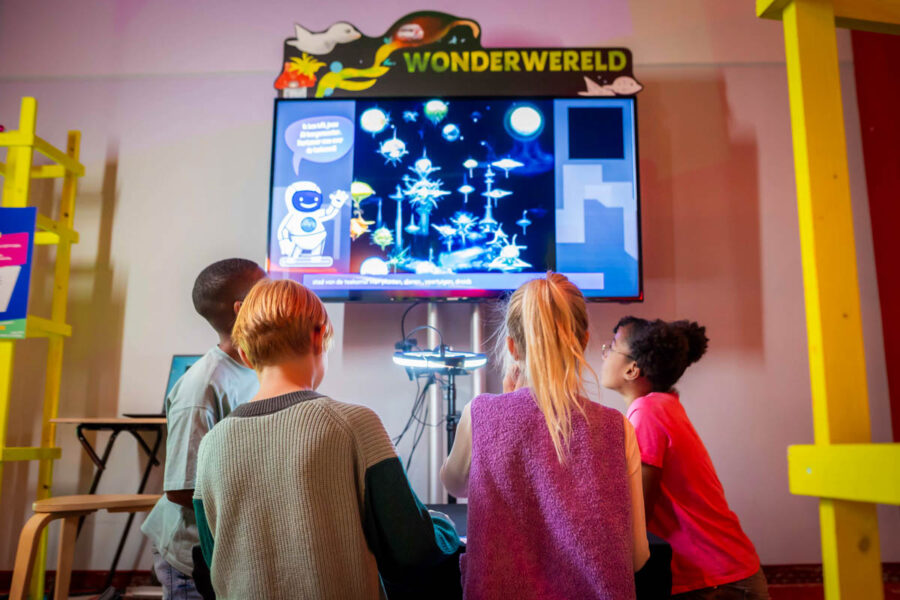 FS_WonderWereld_2 Kinderen bekijken een fysiek kunstwerk van snippers papier dat door AI wordt getransformeerd naar een digitale wonderwereld.